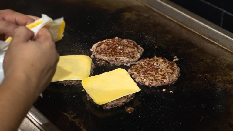 Fatias de queijo sobre os hambúrgueres na chapa
