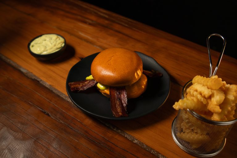Hambúrguer com bacon e cesta de batatas crinkle sobre tábua de madeira