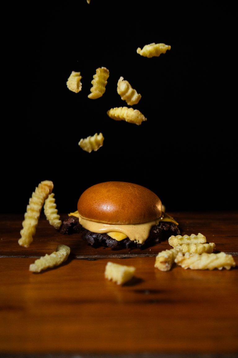 Hambúrguer artesanal com batatas crinkle voando sobre fundo escuro